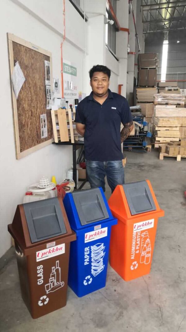 A man smiling with three Upekkha recycle bins in brown, blue and orange.