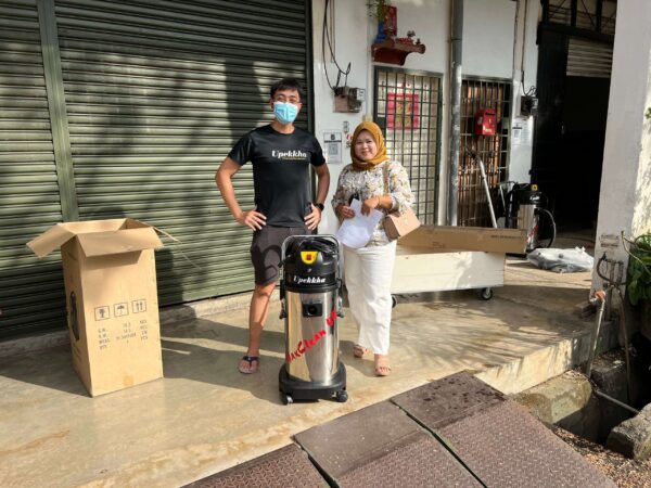 A malay woman posing with a Upekkha salesperson in black t shirt on her newly purchased Upekkha MaxClean carpet and upholstery machine infront of Upekkha's headquarters.