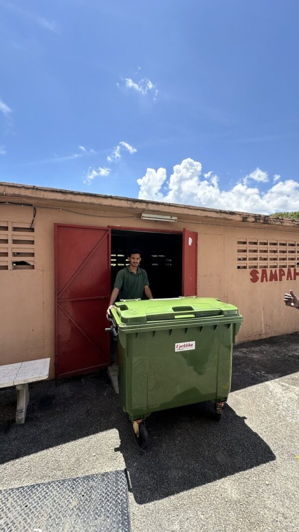 Person pushing green trash bin outside