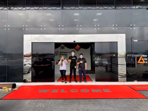 3 people giving the thumbs up with a big red welcome floor mat.