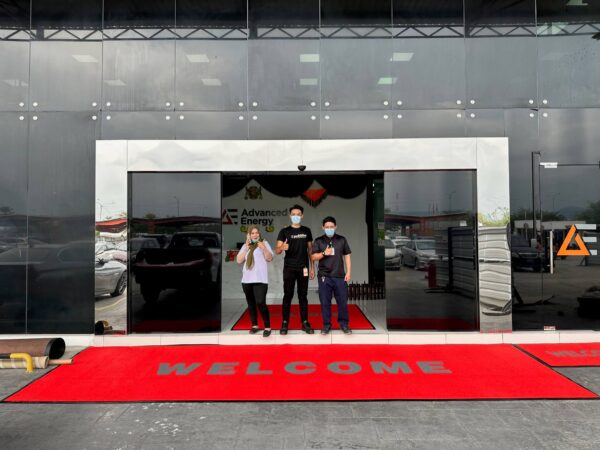 Three people giving the thumbs up with a big red welcome floor mat.